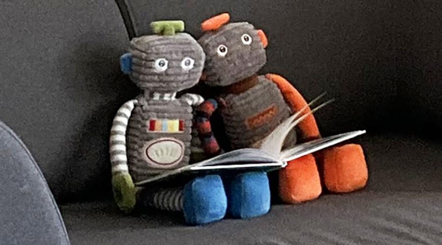 Mjuka robotdockor läser bok i soffa.
