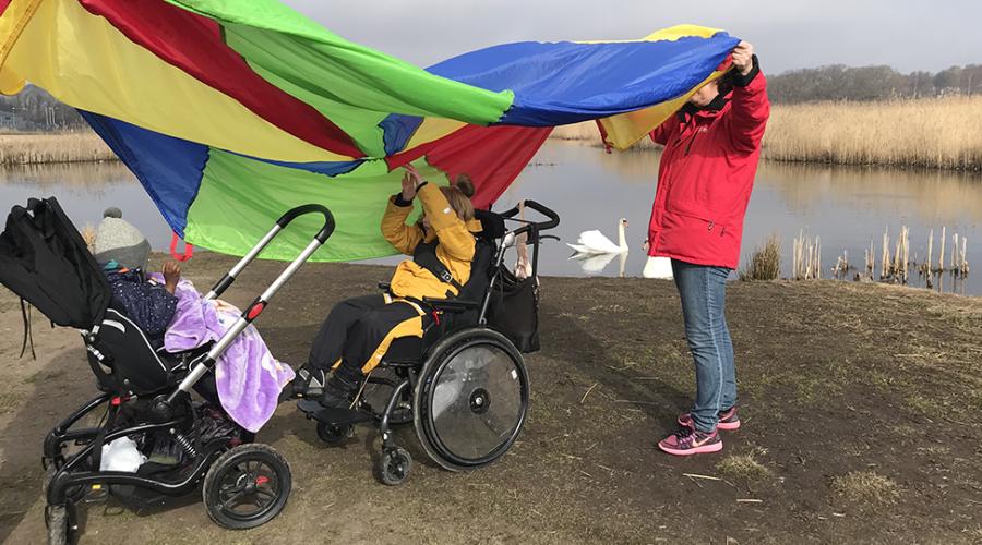 Pedagoger håller färgglad skärm över förskolebarn vid naturområdet Hökällan.