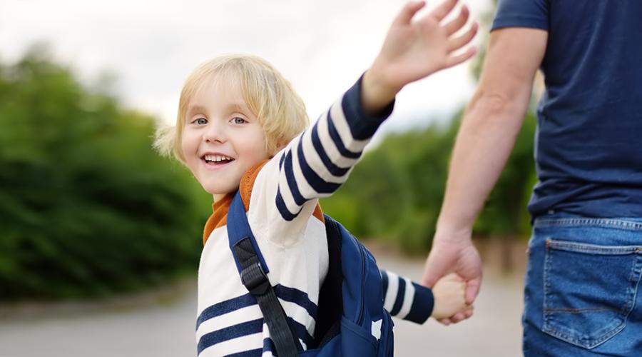 Förskolebarn vinkar hejdå och går iväg med sin pappa.