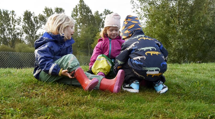 Tre förskolebarn i lek på gräsmatta