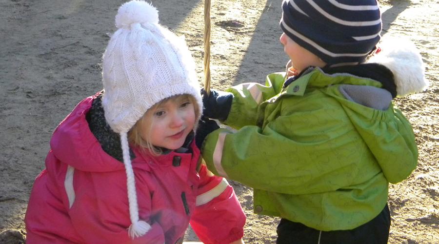 två barn gungar på förskolegården