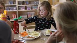 Lunch på förskolan. Ett barn tar grönsaker ur ett fat.